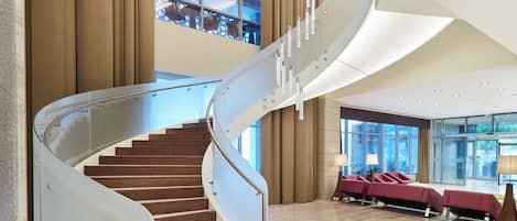 Un moderno vestíbulo de hotel con una escalera espiral, zona de estar y ventanas amplias.