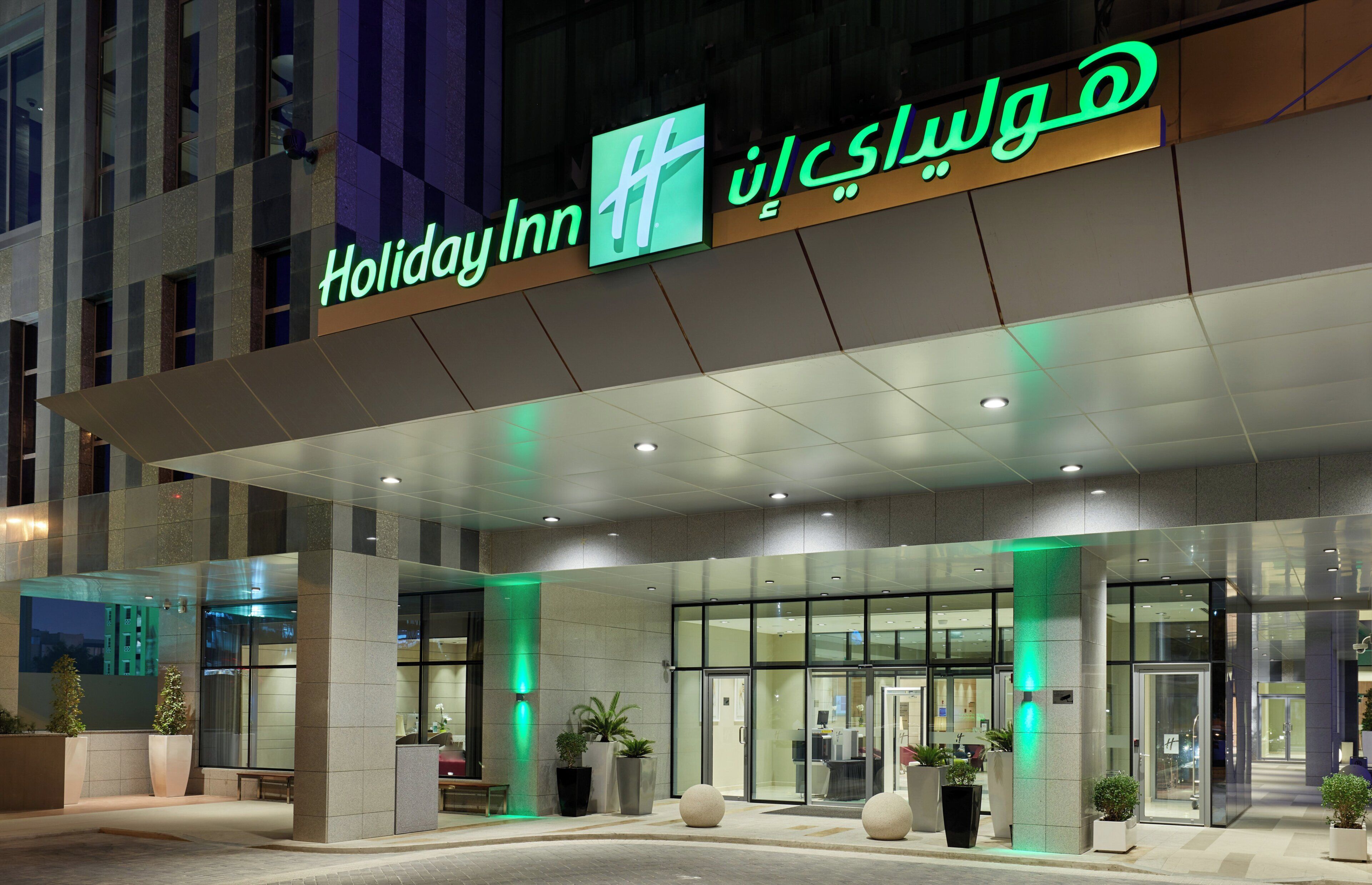 A Holiday Inn hotel entrance with a modern design, featuring a large glass facade and illuminated signage.