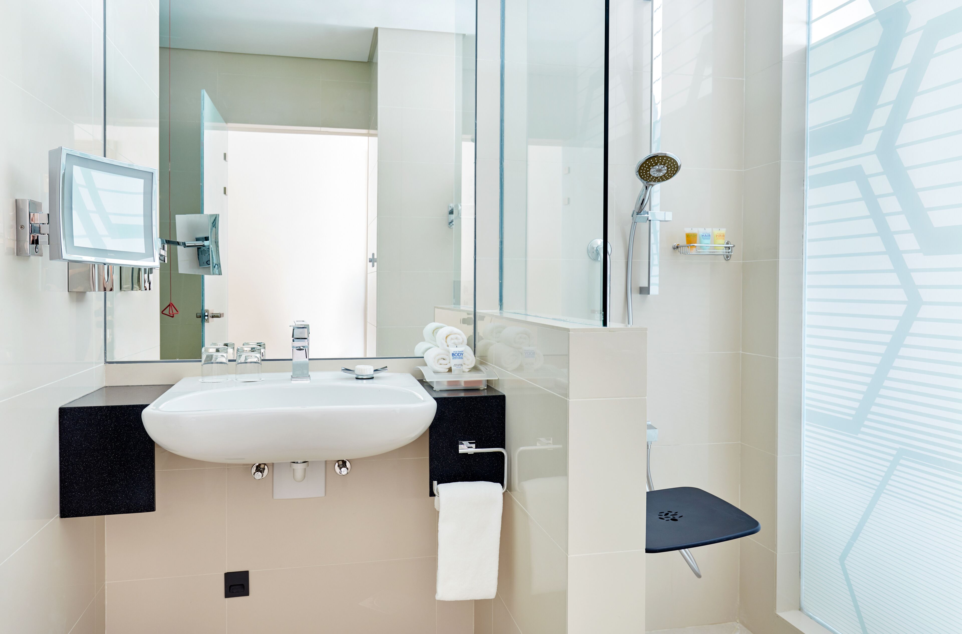 A modern bathroom with a white sink, black countertop, glass shower enclosure, and a glass shower door.