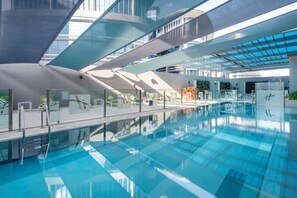 A modern indoor swimming pool with clear blue water, surrounded by glass walls and a contemporary architectural design.