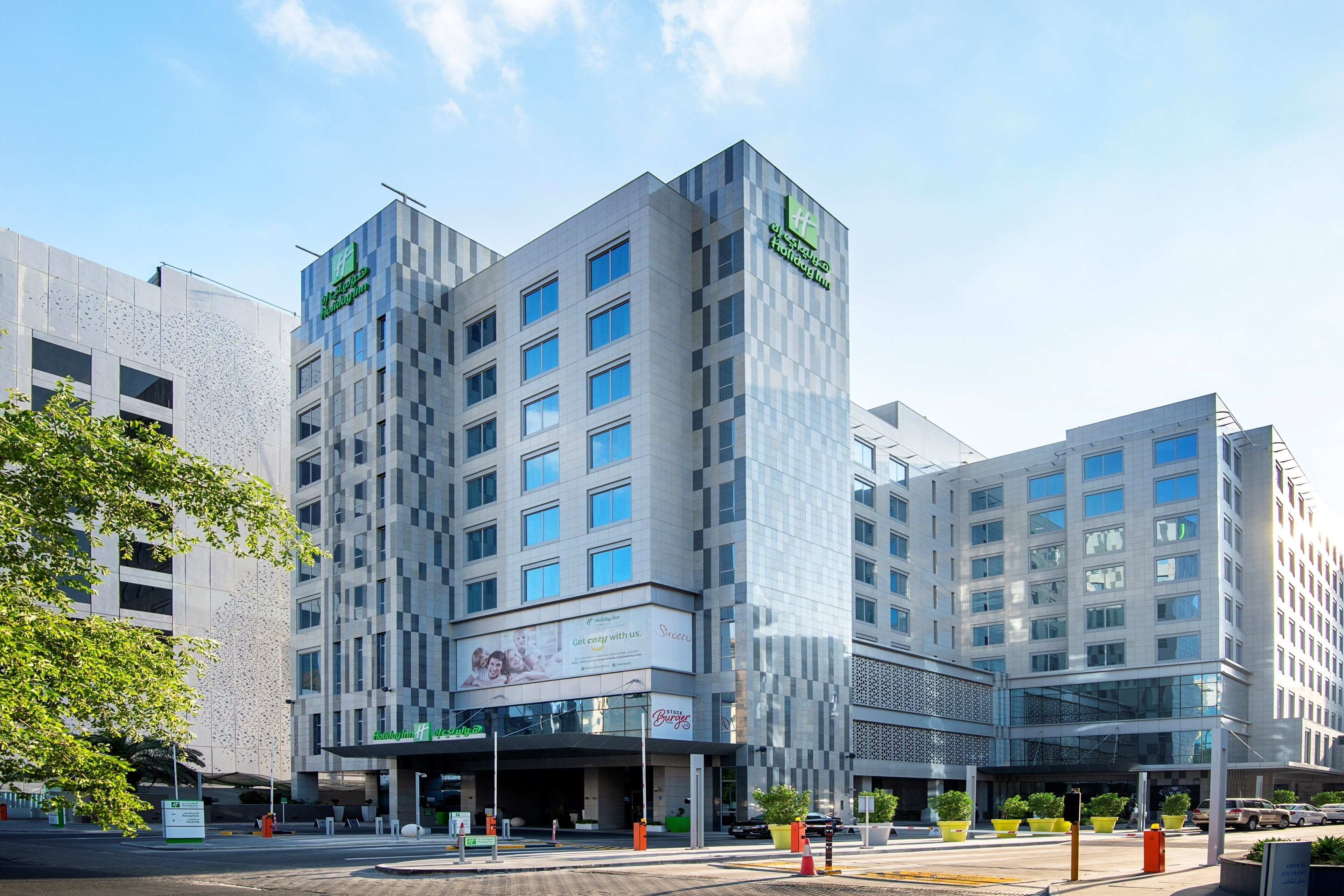 Ein mehrstöckiges Holiday Inn Hotel mit modernem Design, das eine markante Einfahrt und eine große Glasfassade aufweist.