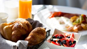 A breakfast setting with croissants, a bowl of fruit, and a glass of orange juice.