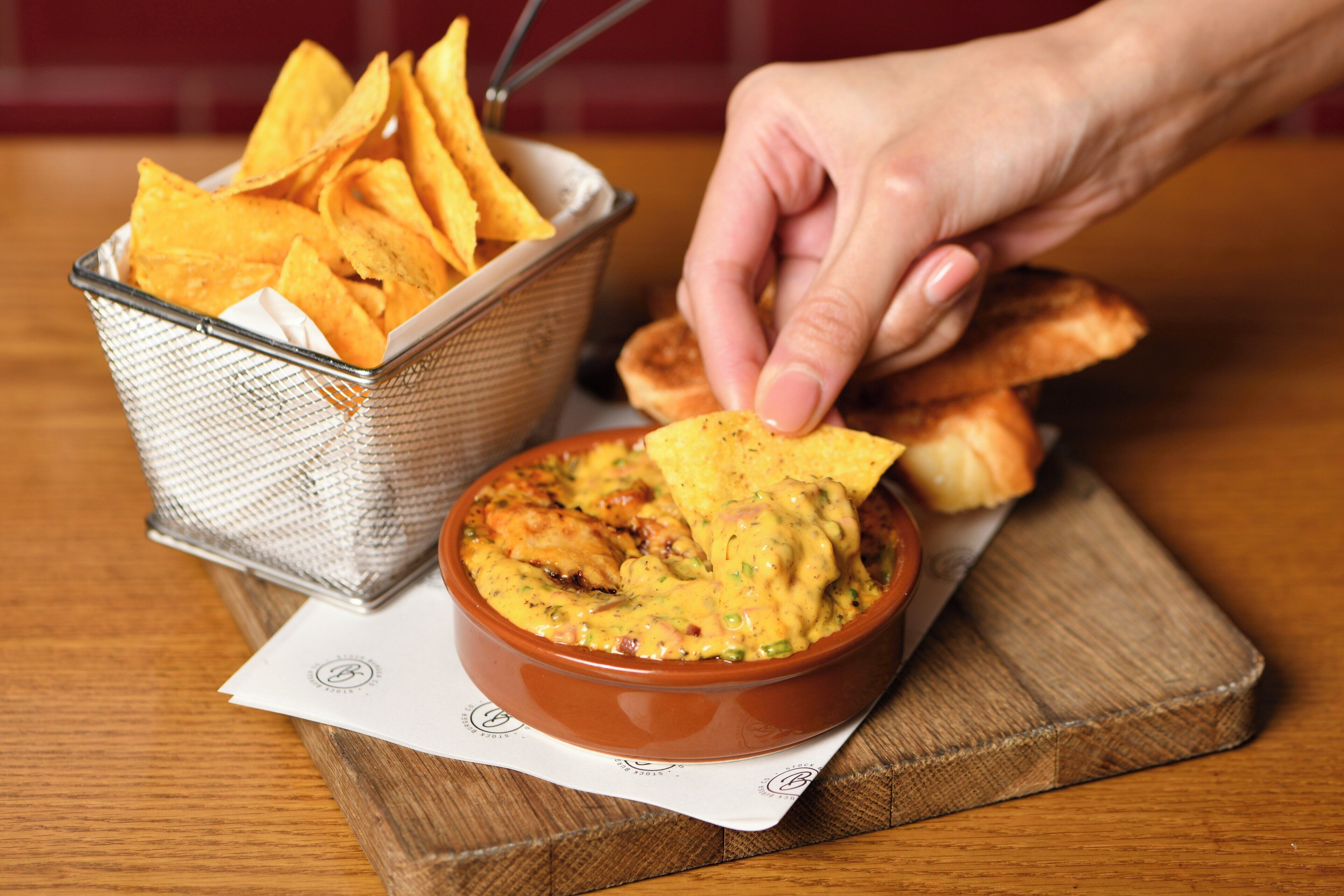 Un bol de trempette avec des chips de tortillas et une main qui prend une chip pour la tremper.