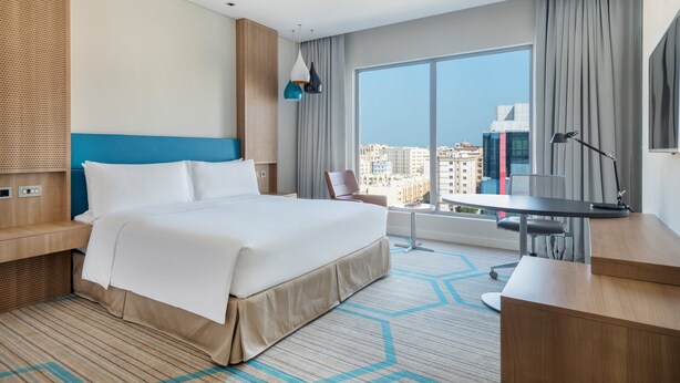 A modern hotel room with a large bed, a desk, and a view of the city.