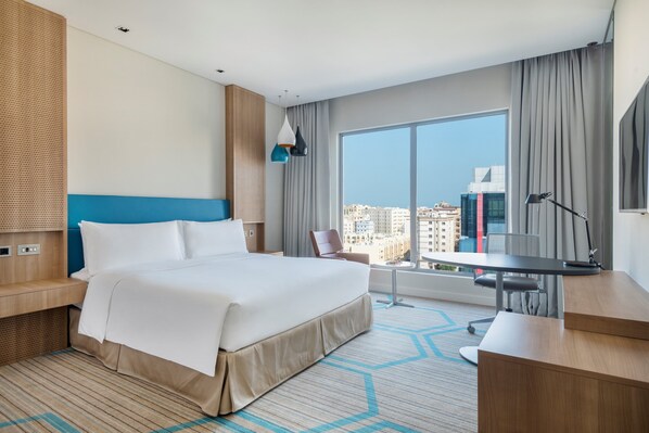 A modern hotel room with a large bed, a desk, and a view of the city.