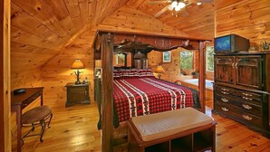 Ein Schlafzimmer in einer Blockhütte mit einem Himmelbett, Holzmöbeln und einem Fernseher auf einem Schrank.