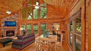 Ein Holzblockhaus-Interieur mit Kamin, Fernseher, Essbereich und großen Fenstern.