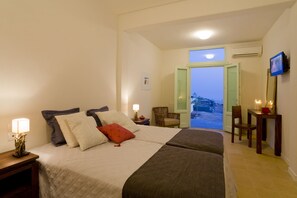 A hotel room with a bed, a chair, a table, and a TV. - Blackrock Villa (Santorini)