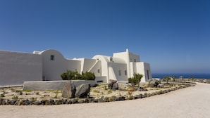 Un edificio blanco con techo curvo, rodeado de rocas y vegetación escasa.