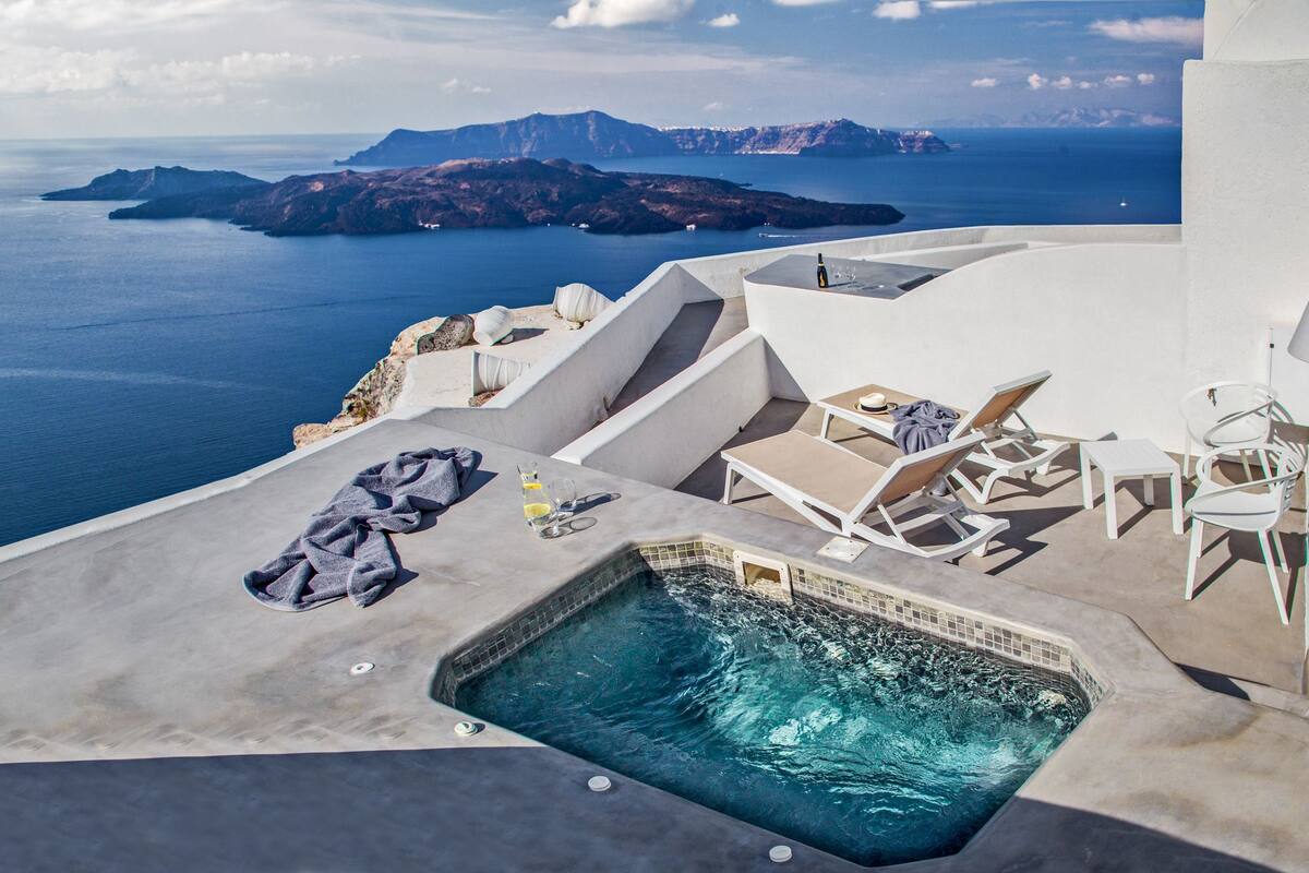 A rooftop pool with lounge chairs and a bottle of wine, overlooking a scenic view of the sea and islands.