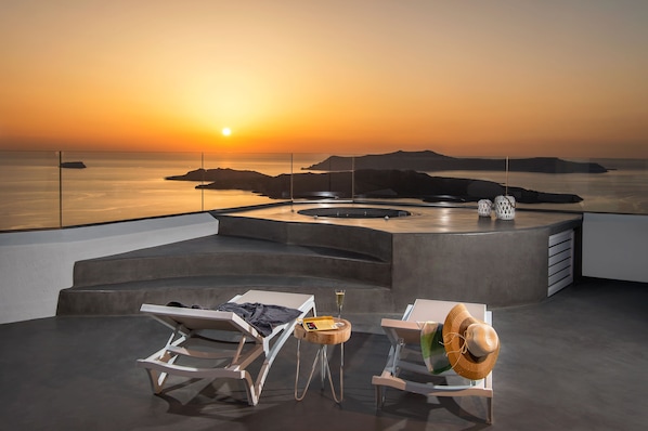 A sunset view from a rooftop terrace with lounge chairs, a drink, and a straw hat. - Villa Irini Fira Adults Only (Santorini)