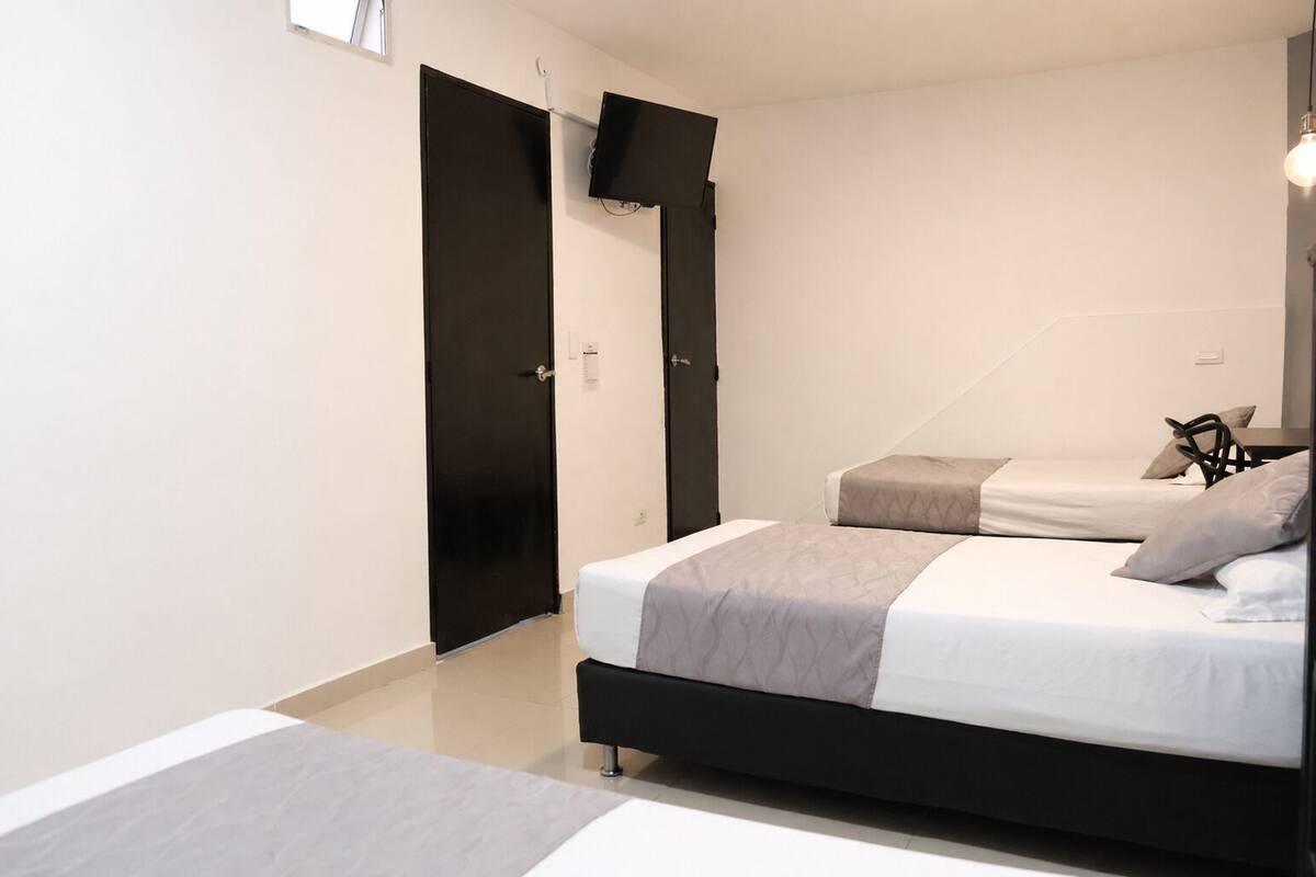 Un dormitorio con dos camas, un armario negro, un televisor de pantalla plana y una lámpara.