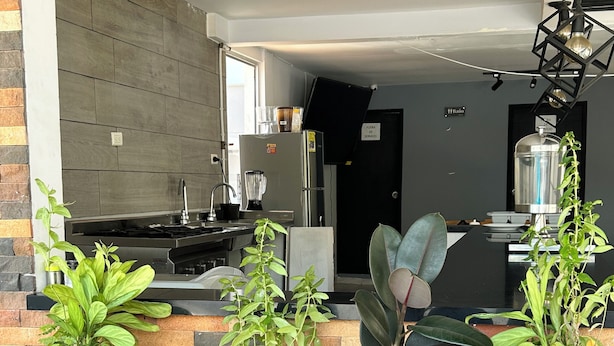 A modern kitchen with a brick wall, a dining area with a white table, and potted plants. - Hotel Palmas Del Estadio (Medellín)