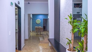 A hallway with a marble floor, a clock on the wall, and potted plants. - Hotel Palmas Del Estadio (Medellín)