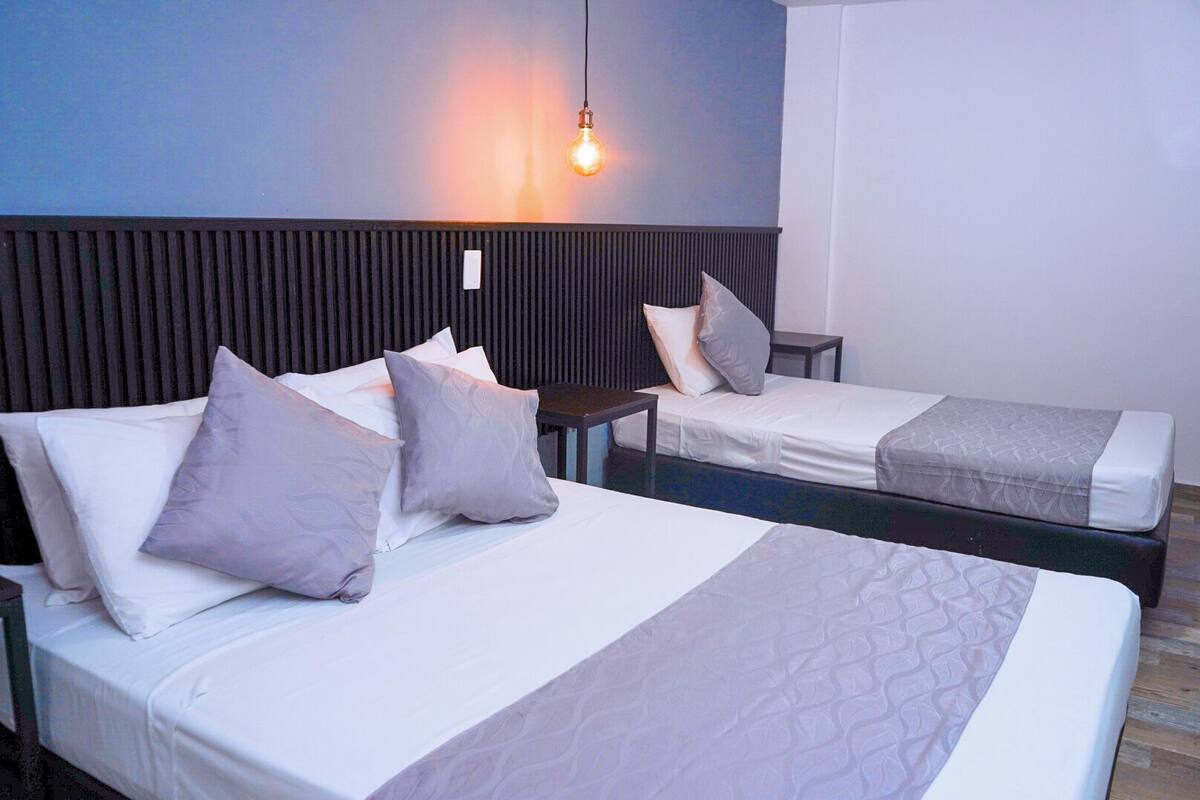 Habitación de hotel con dos camas, una mesita de noche, una lámpara fijada a la pared y suelo de madera.