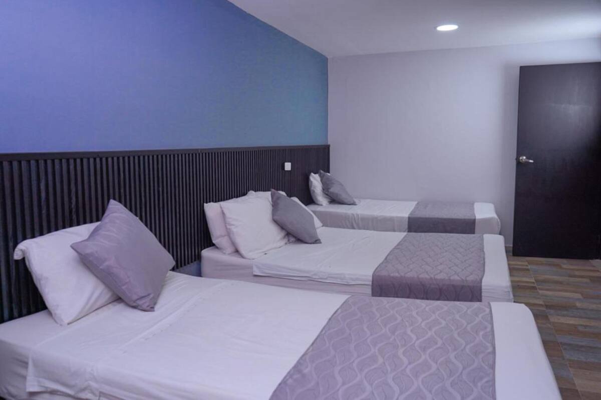Habitación de hotel con tres camas individuales, cada una con almohada y manta.