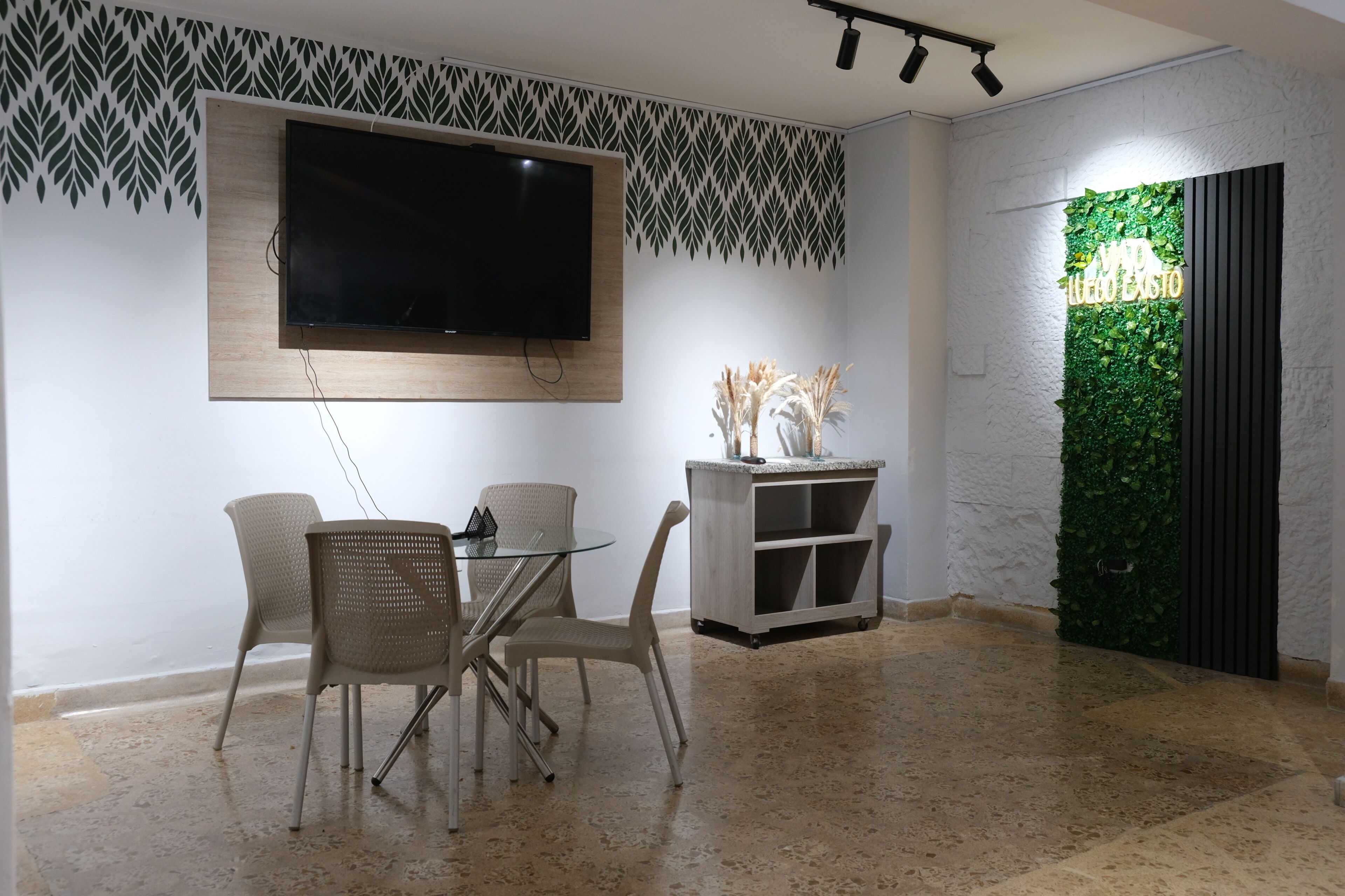 Un comedor con televisor, sillas, mesa y decoración en la pared.