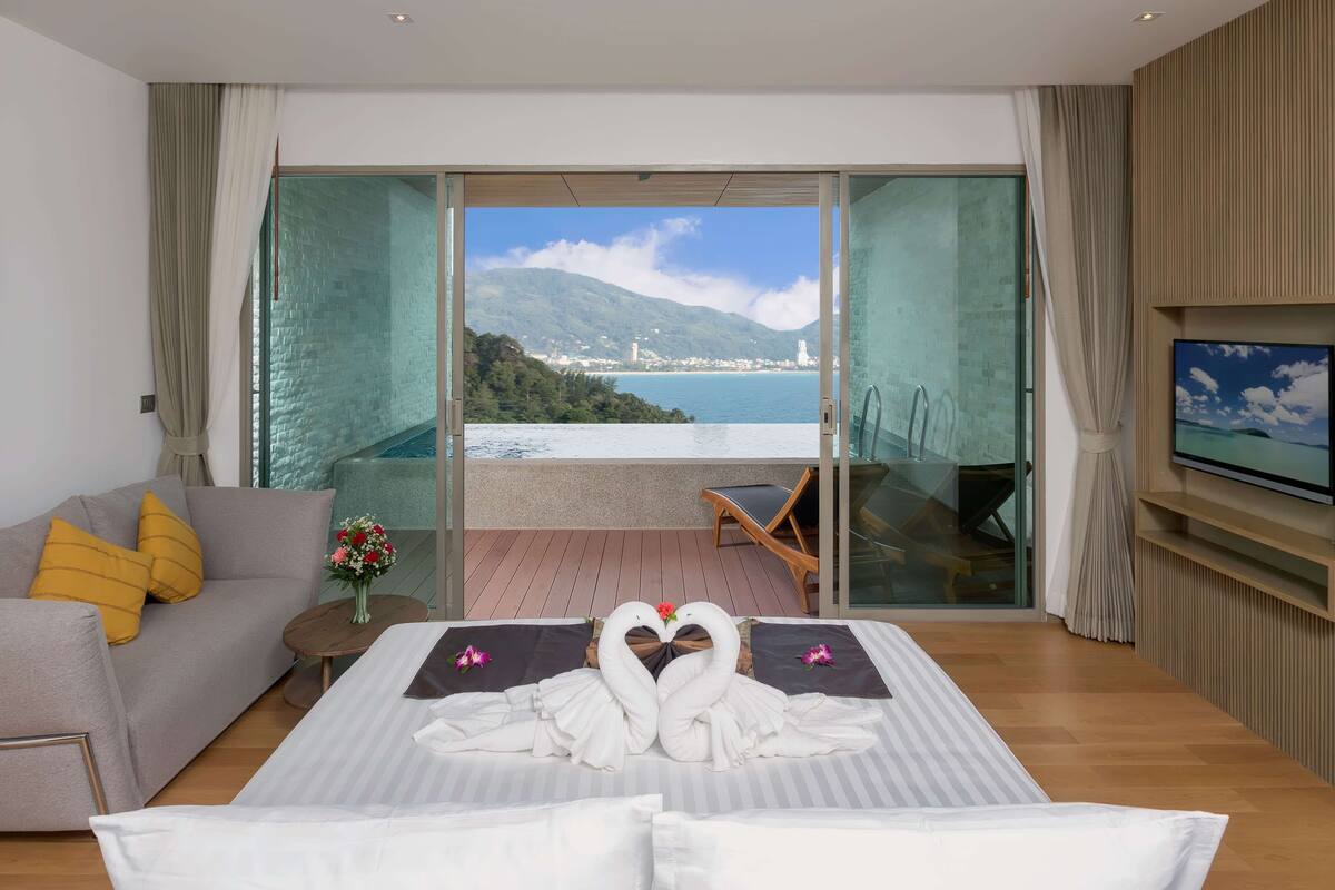 Une chambre d’hôtel comprenant un lit, un canapé, une télévision et un balcon avec vue sur la mer et les montagnes.