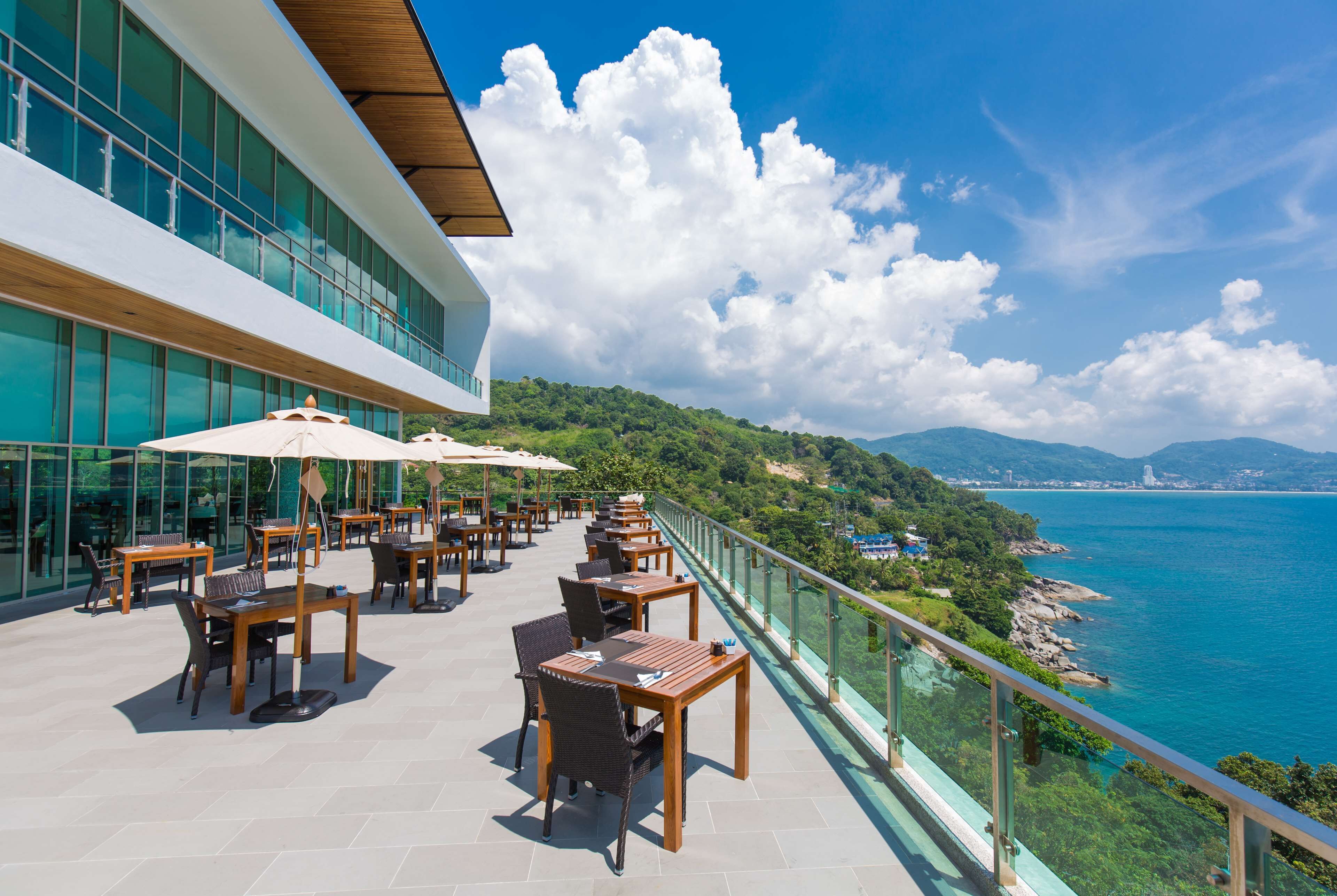 A rooftop terrace with outdoor seating and a glass railing overlooking a coastal view.