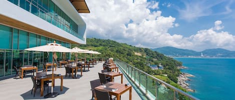 A rooftop terrace with outdoor seating and a glass railing overlooking a coastal view.