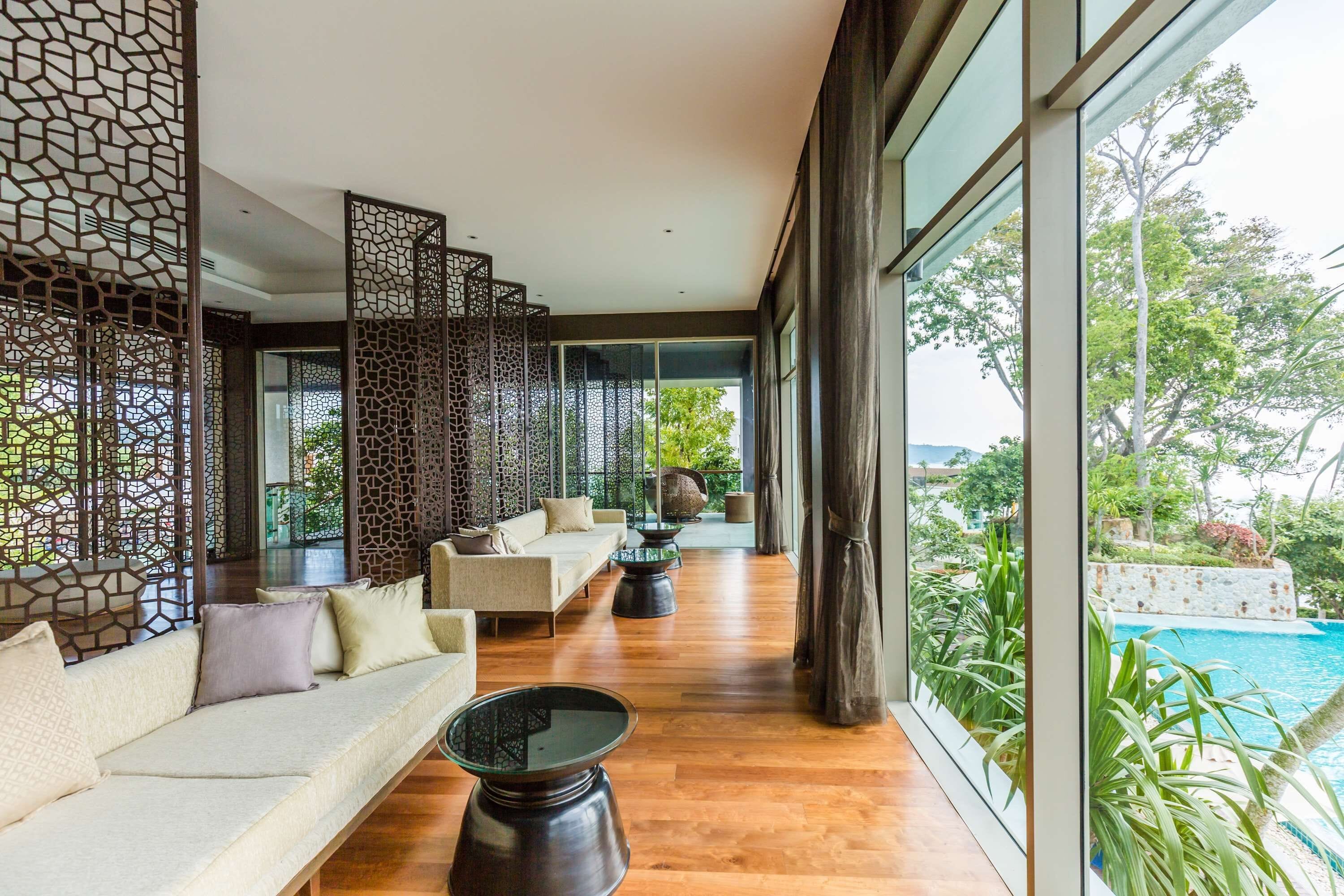 Un espacio interior moderno con suelo de madera, un conjunto de sofás, una mesa de centro y vistas a una piscina a través de amplios ventanales.