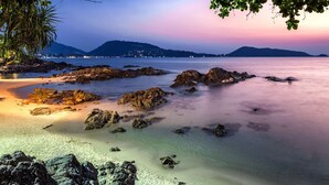 A beach with clear water, rocks, and a distant mountain range.