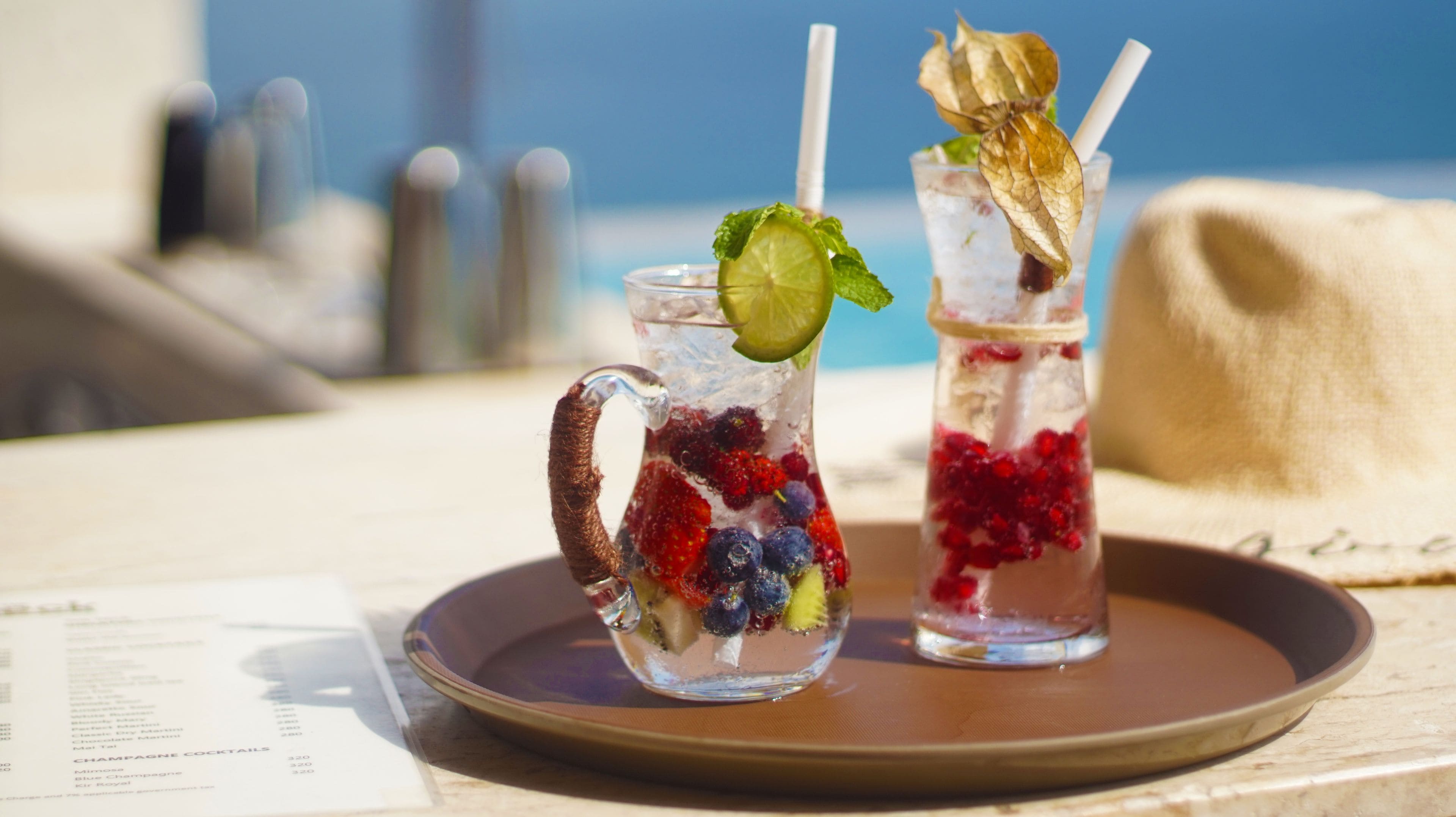 Two iced drinks with fruit and mint on a tray.