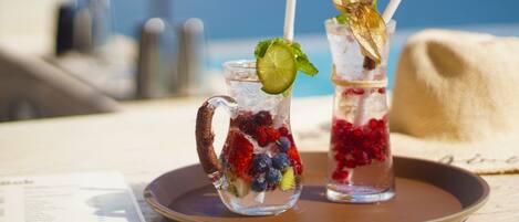 Two iced drinks with fruit and mint on a tray.