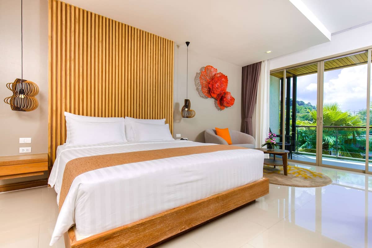 A modern bedroom with a large bed, a wooden slatted headboard, a decorative wall piece, and a view of greenery through large windows.