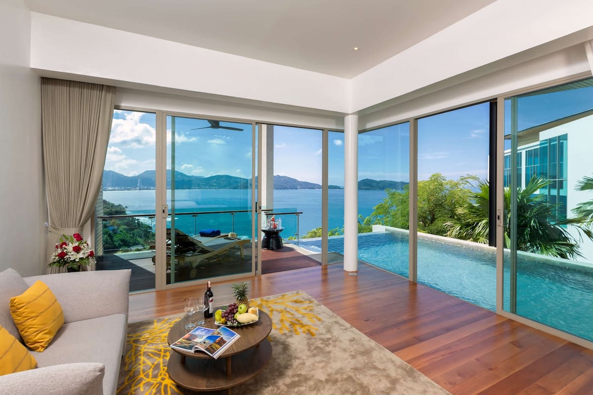 A modern living room with a large glass door leading to a balcony overlooking a pool and a scenic view of the sea.
