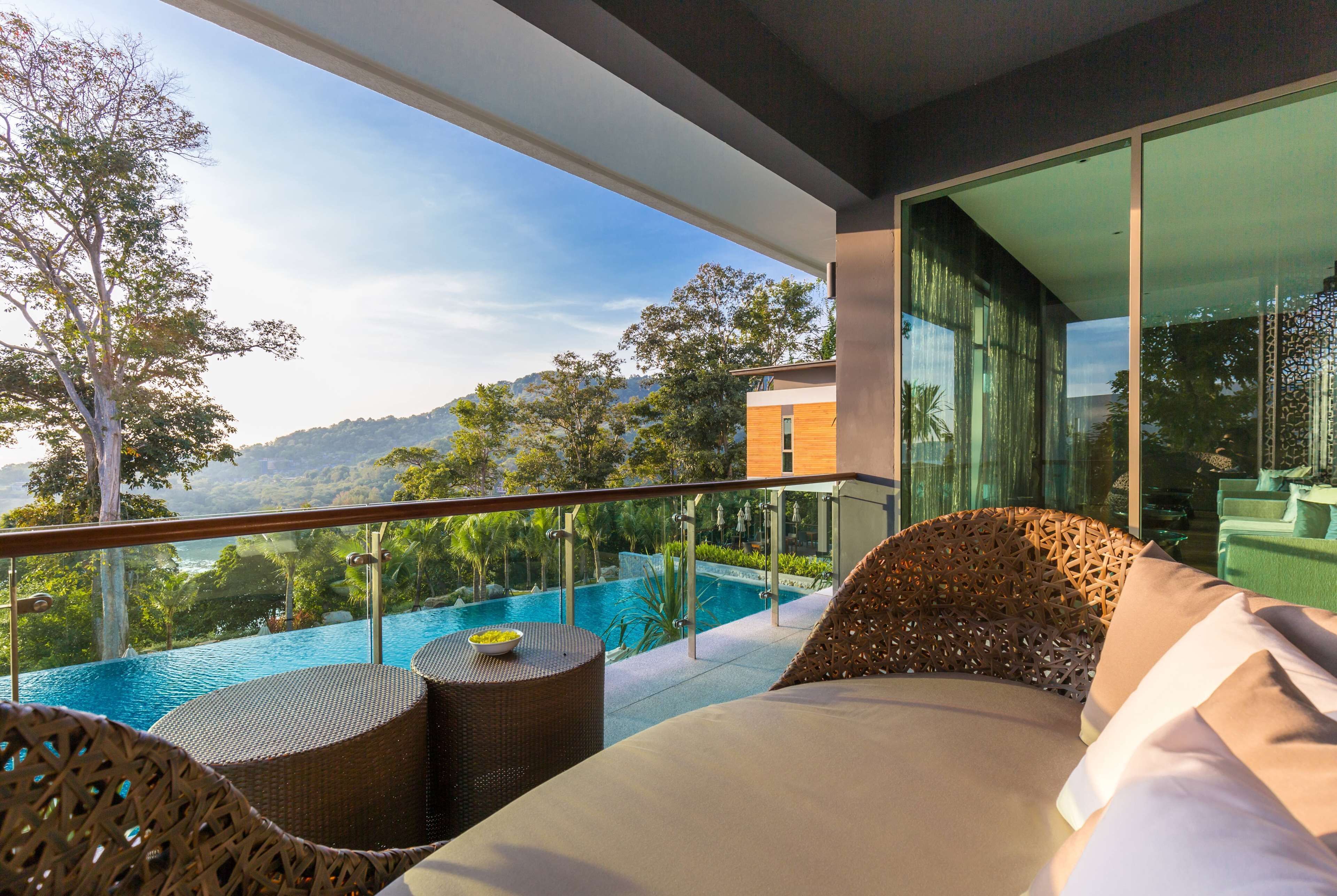 Un balcon donnant sur une piscine, avec des meubles en osier et une balustrade en verre.