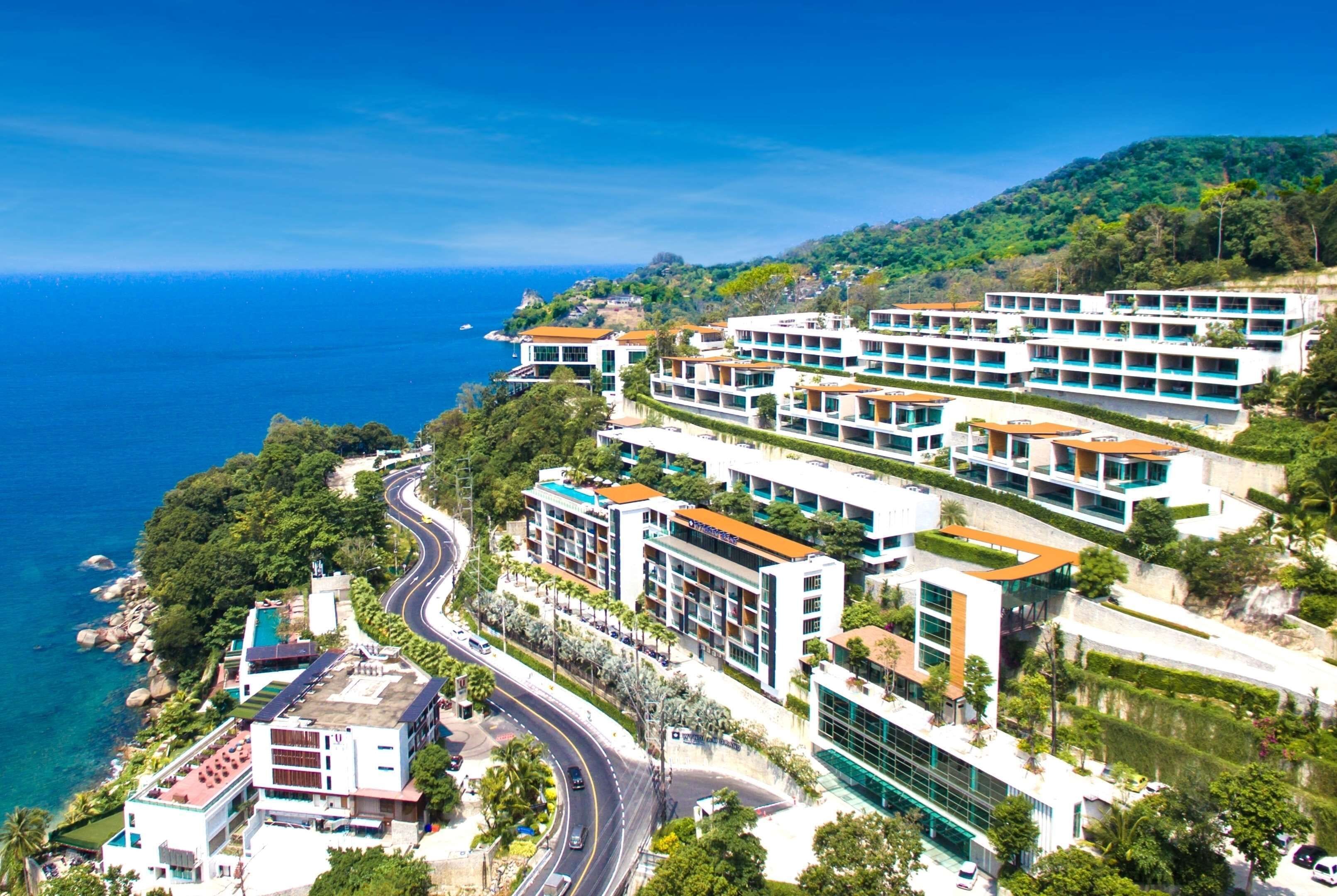 A coastal hotel with multiple buildings, a winding road, and a view of the sea.