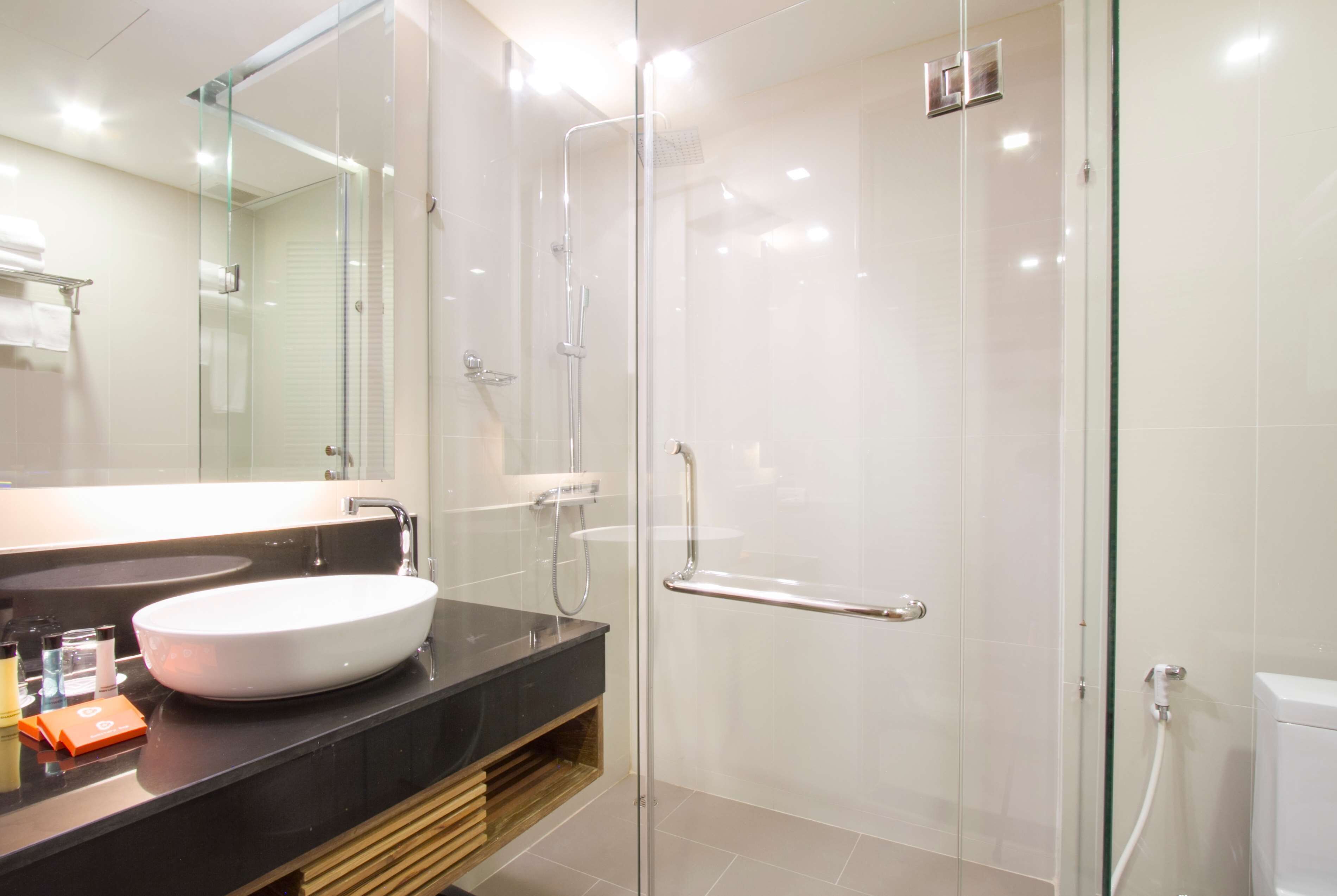 A modern bathroom with a glass-enclosed shower, a large mirror, and a black countertop with a white sink.