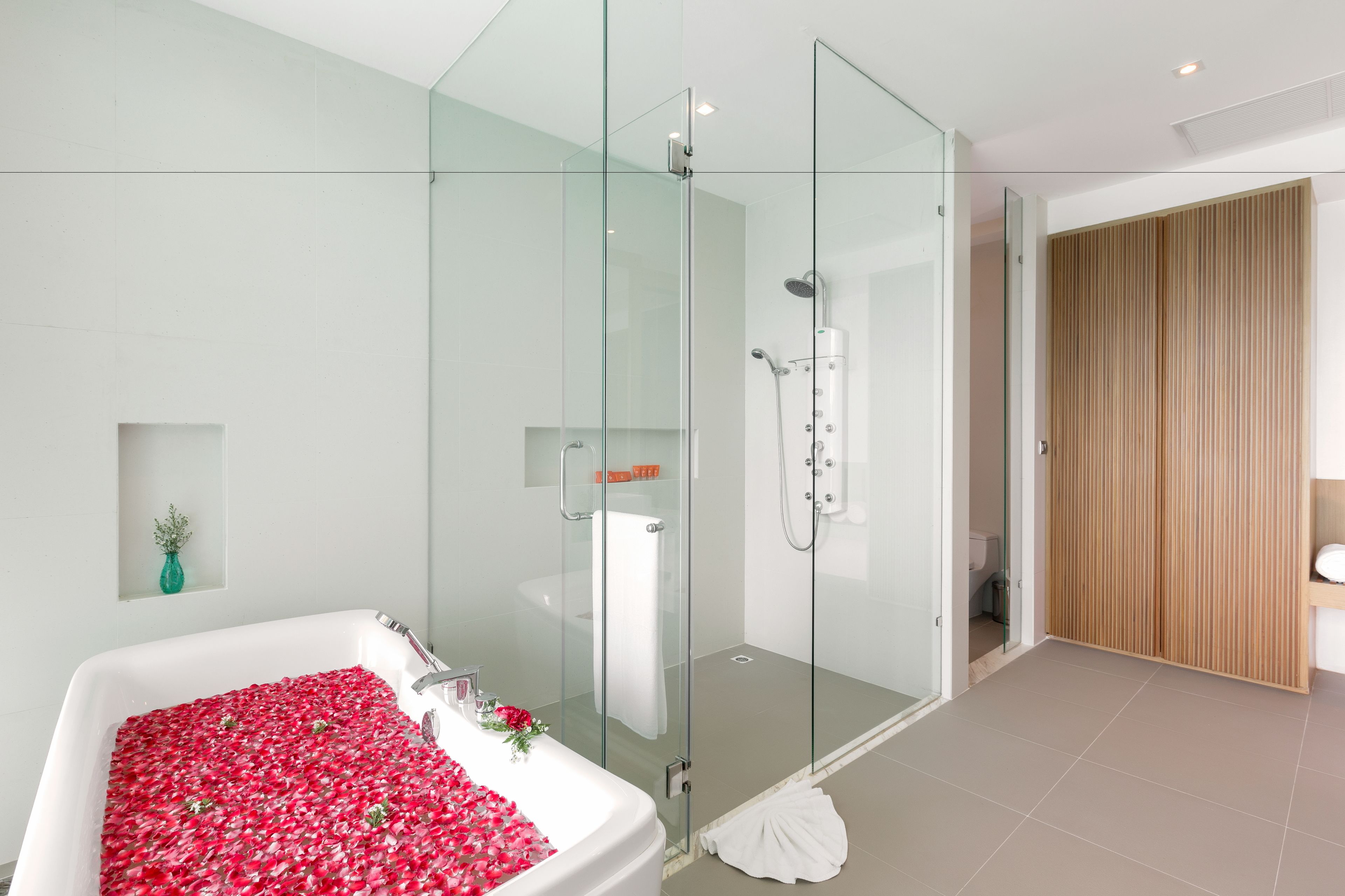 Une salle de bain moderne avec une douche à parois de verre, une baignoire remplie de pétales de roses et une armoire en bois.