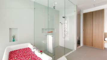 A modern bathroom with a glass-enclosed shower, a bathtub filled with rose petals, and a wooden wardrobe.