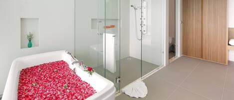 A modern bathroom with a glass-enclosed shower, a bathtub filled with rose petals, and a wooden wardrobe.