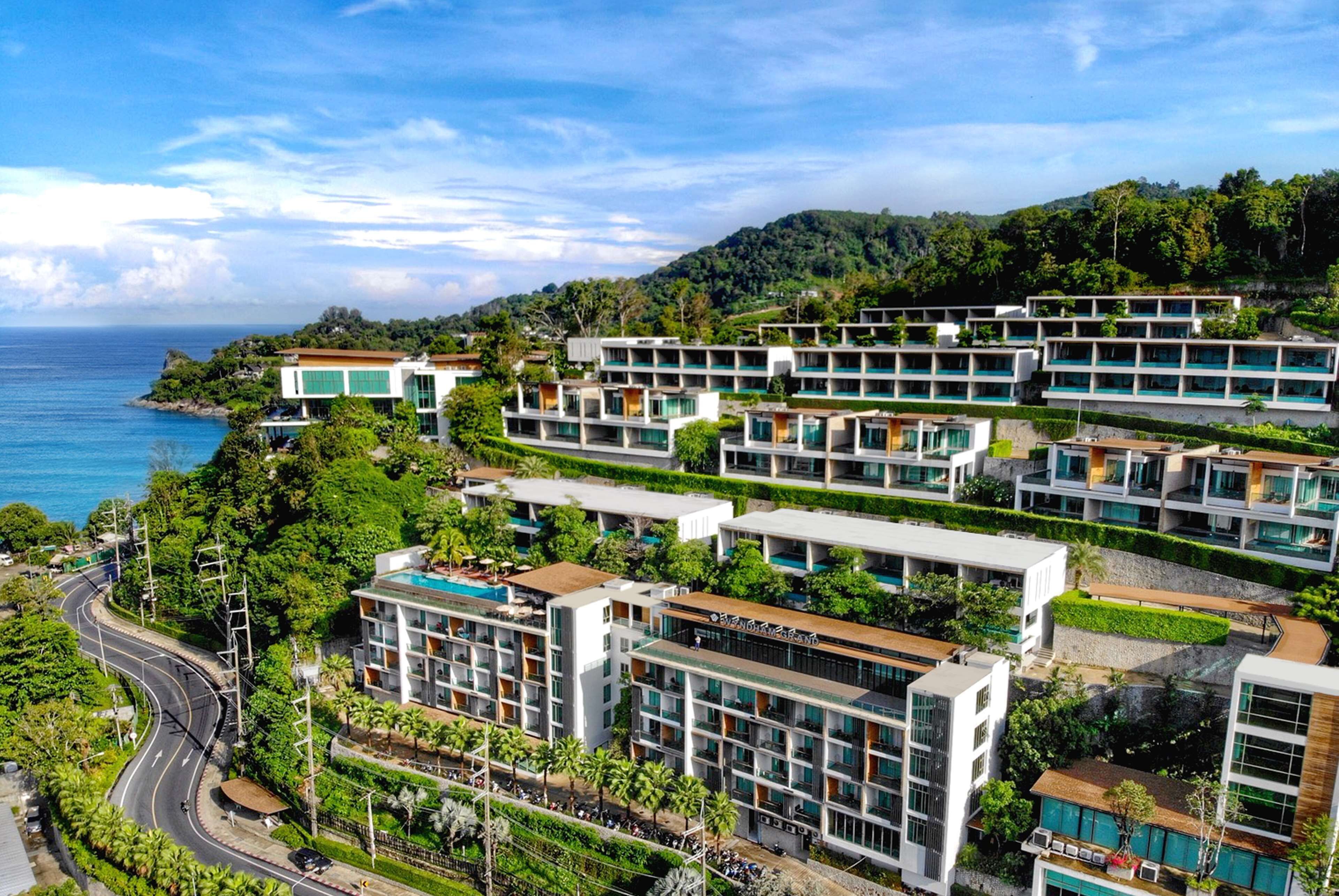A modern hotel complex with multiple buildings, a curved road, and a view of the sea.