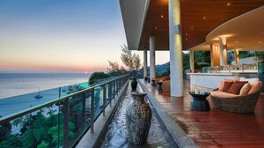 A modern outdoor lounge area with a view of the sea, a water feature, and a seating area with a wicker sofa and a small table.
