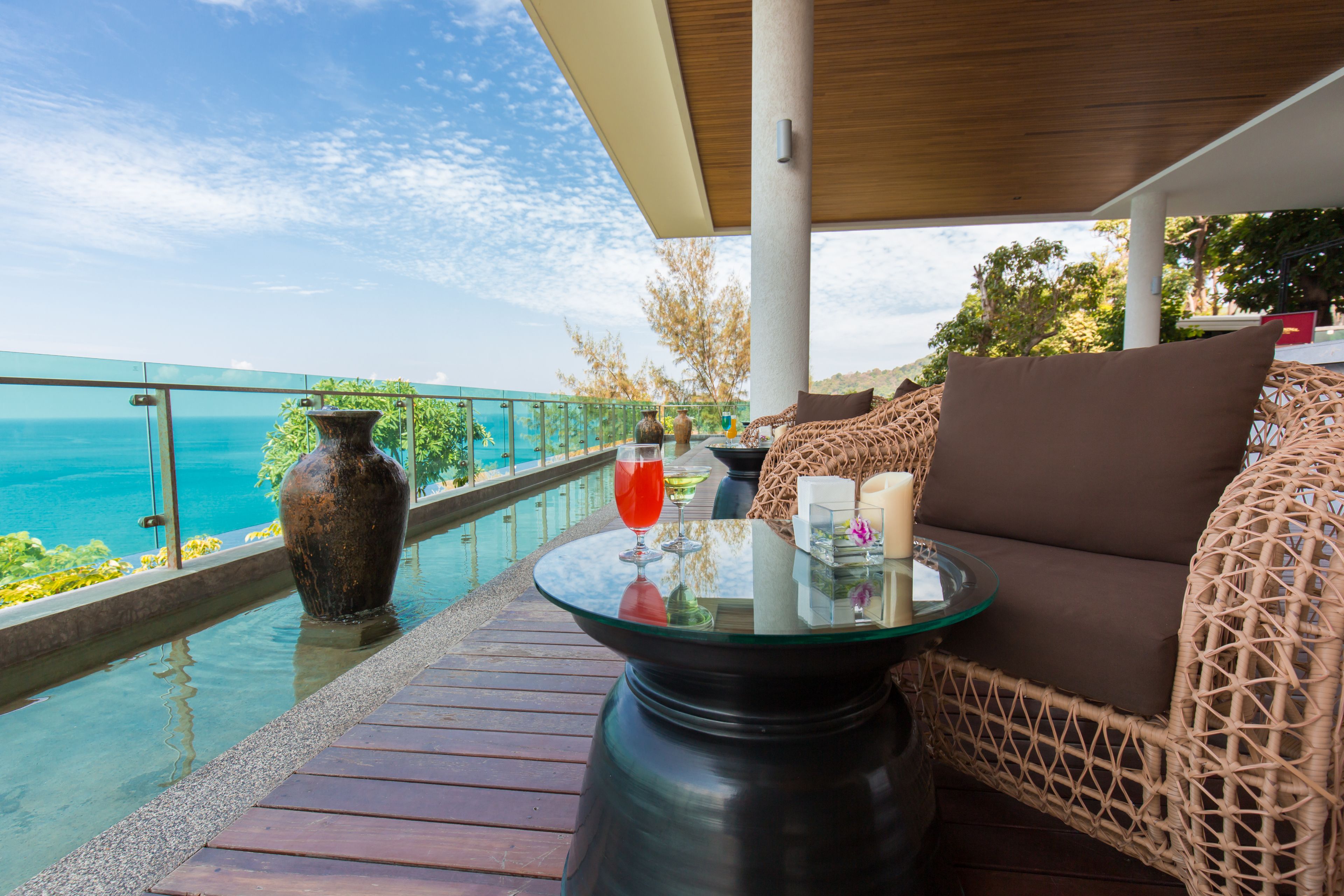 A balcony with a glass table, wicker furniture, and a view of the sea.