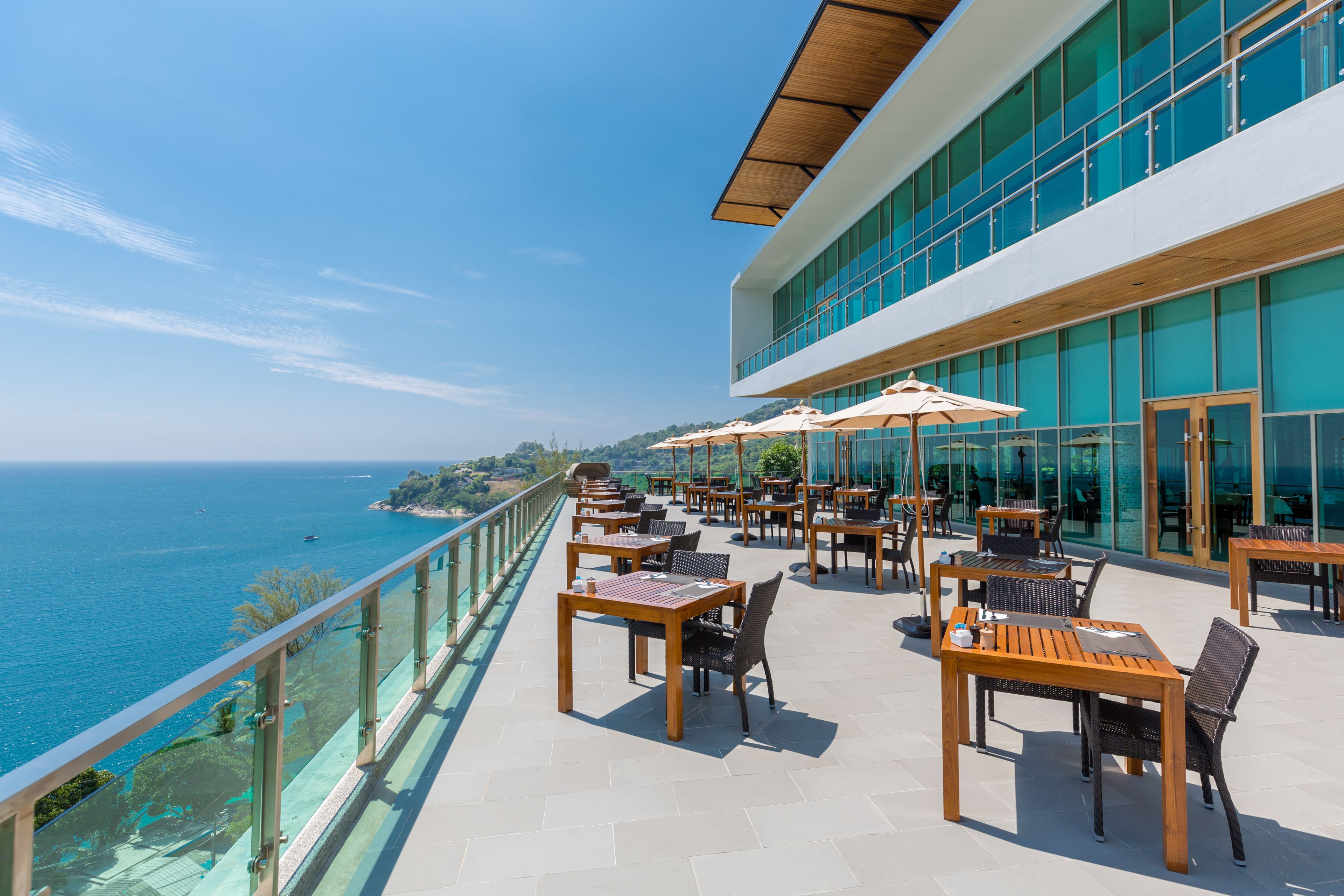 An outdoor terrace with tables and chairs, overlooking a body of water.