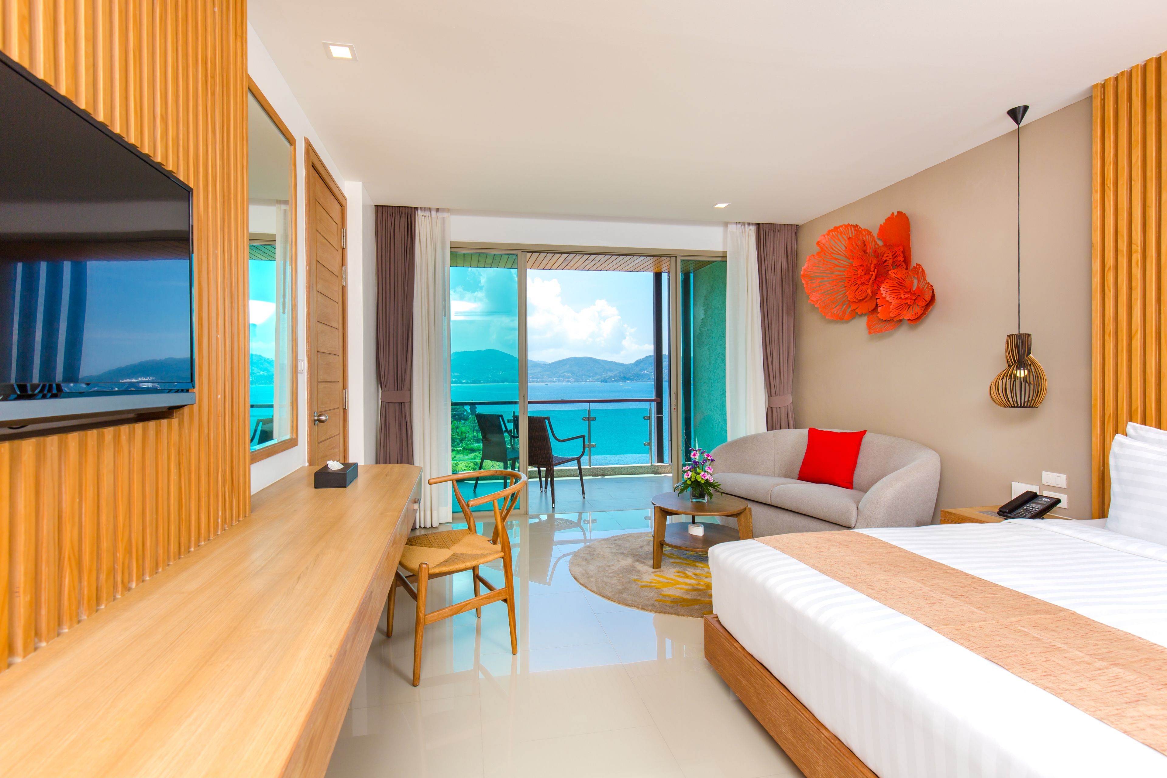 Une chambre d’hôtel moderne équipée d’un lit, d’un canapé, d’une télévision, d’un bureau et d’un balcon offrant une vue sur la mer.