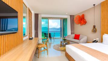 Une chambre d’hôtel moderne équipée d’un lit, d’un canapé, d’une télévision, d’un bureau et d’un balcon offrant une vue sur la mer.