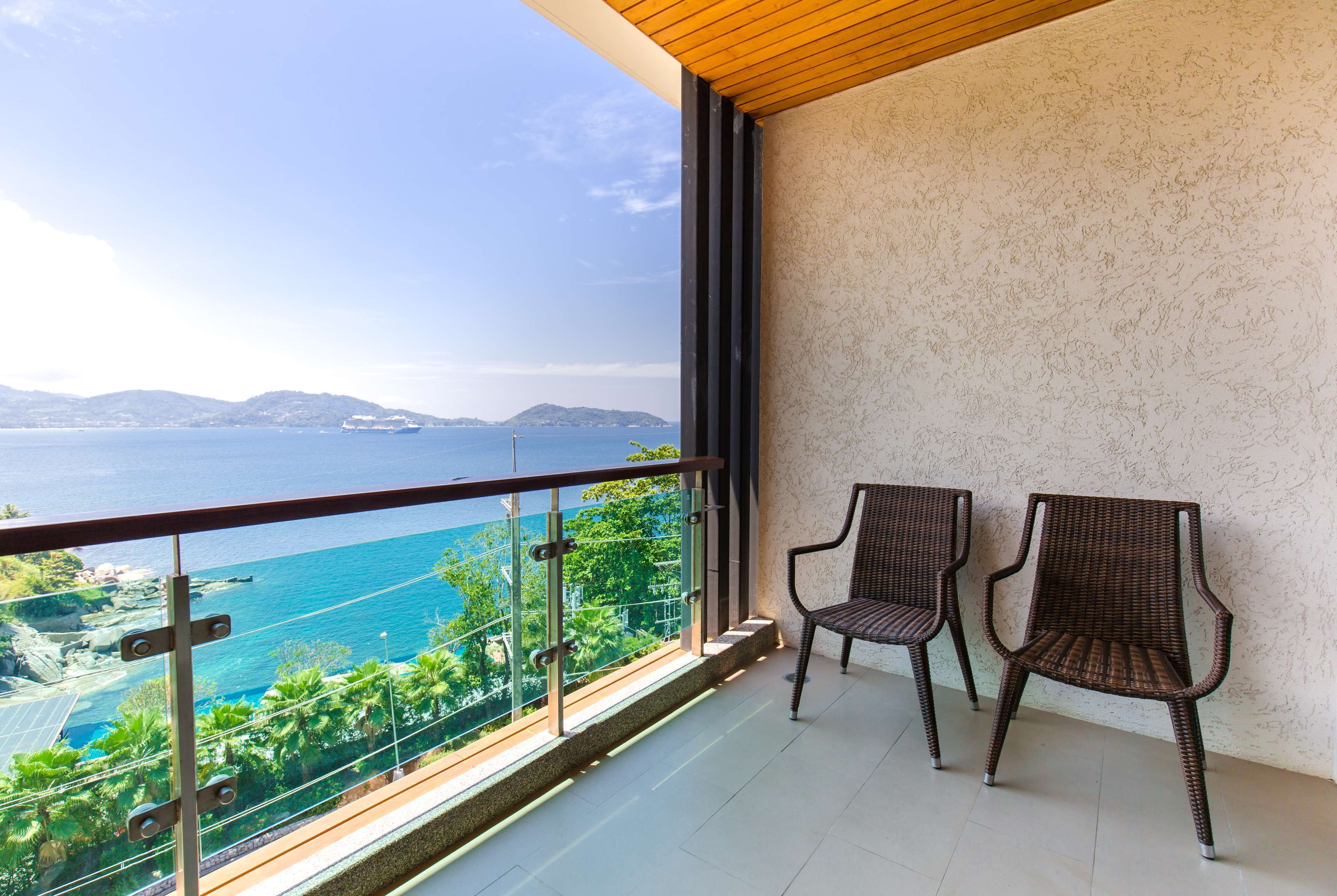 Un balcon avec deux fauteuils en osier, une vue sur la mer et un paysage montagneux.