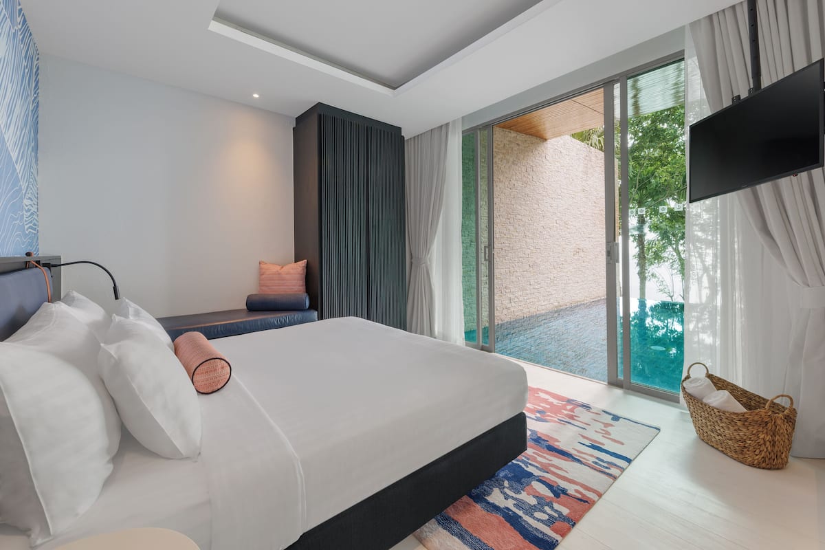 A modern bedroom with a large bed, a flat-screen TV, and a view of the outdoors through a sliding glass door.
