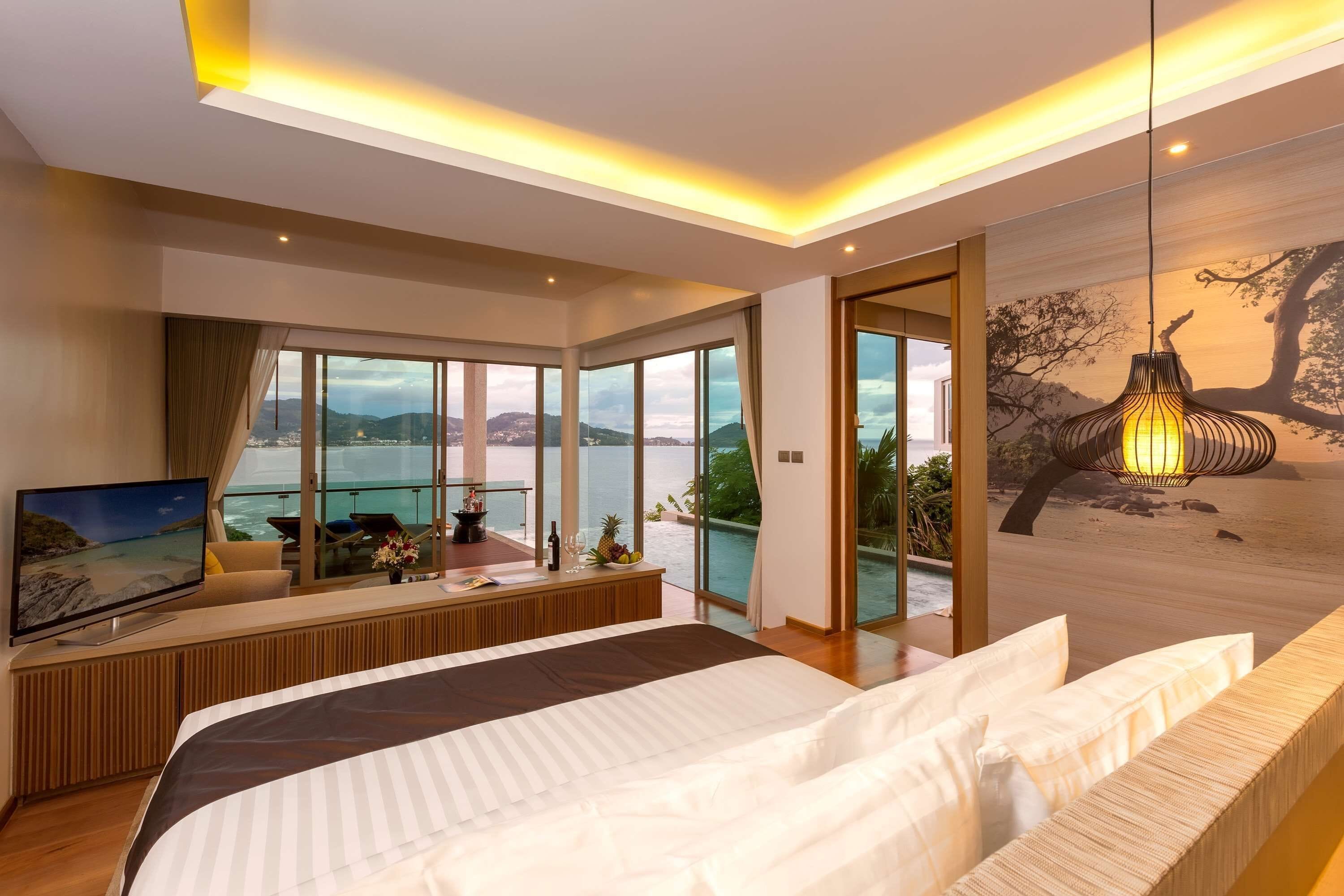 Ein modernes Hotelzimmer mit einem großen Bett, einem Fernseher, einem Balkon mit Meerblick und einer Essecke mit Tisch und Stühlen.