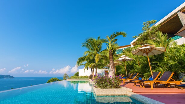 A poolside area with lounge chairs and umbrellas, overlooking a clear blue sky and ocean.