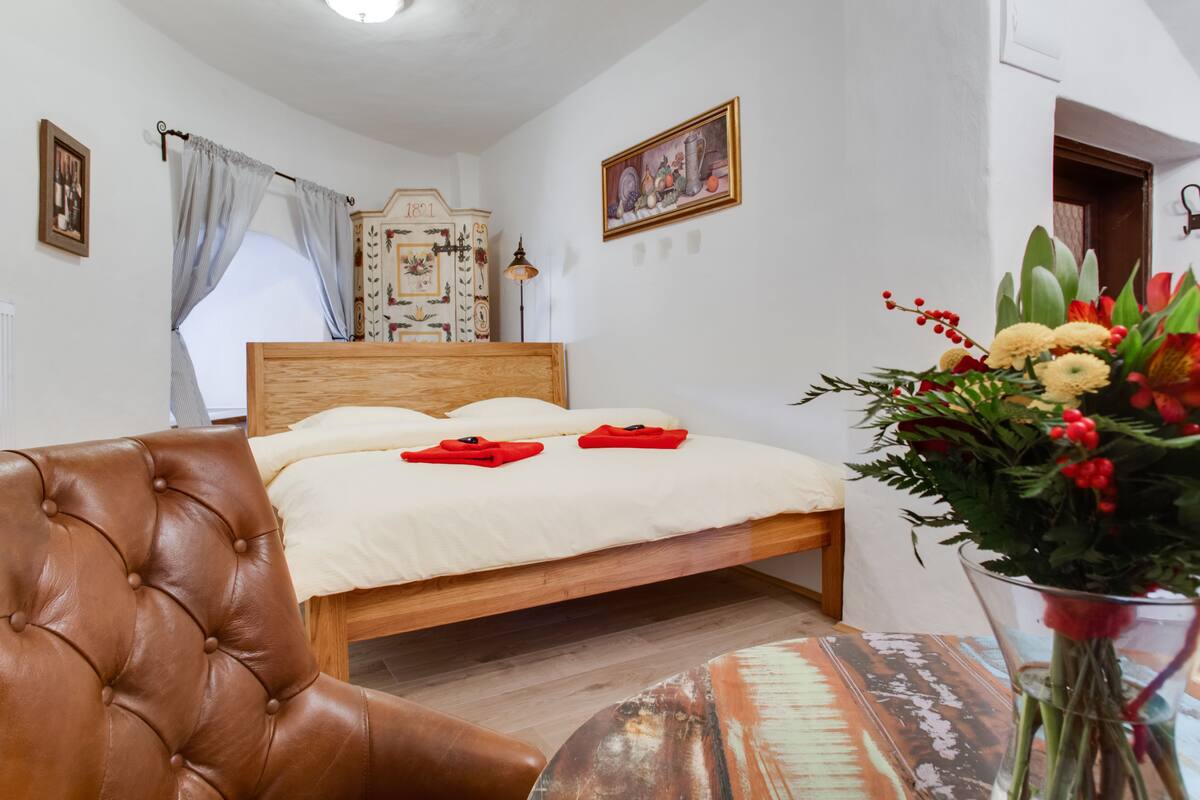 A neatly arranged bedroom with a wooden bed, a leather armchair, and a vase of flowers.