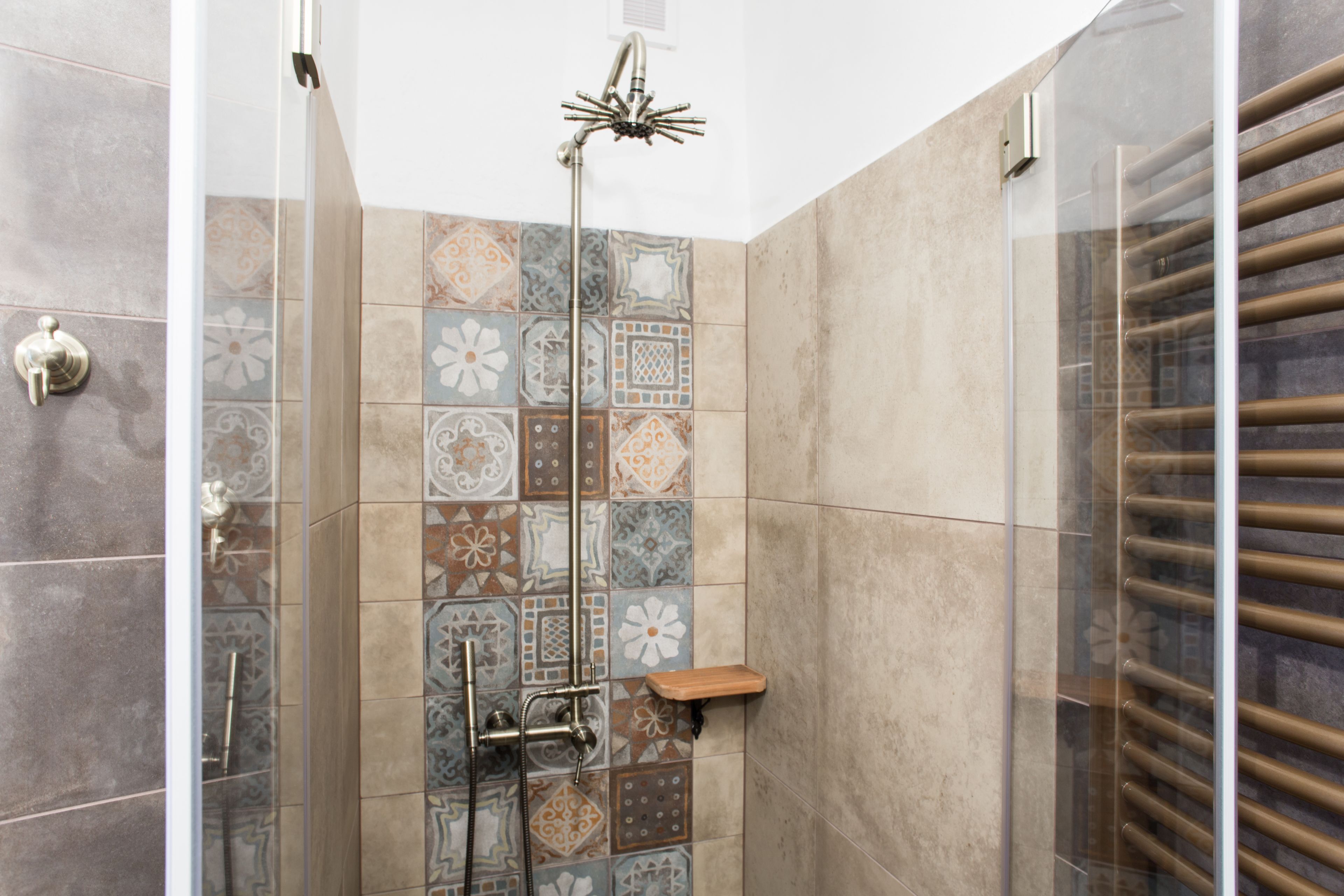 A shower with a glass door, a showerhead, and a wooden shelf.