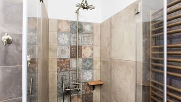 A shower with a glass door, a showerhead, and a wooden shelf.