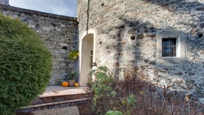 Un edificio de piedra con una ventana pequeña y una puerta, rodeado de plantas y un camino de piedra.